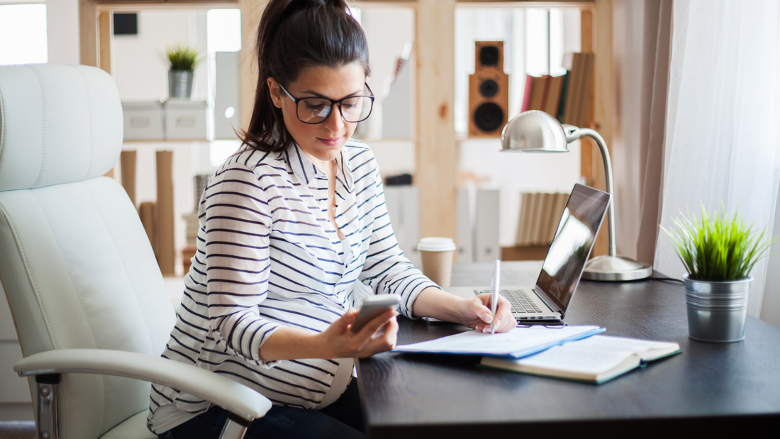 Picture of women sitting at a desk writing a birth plan while using this blog as a guide. She has books and papers on her desk along with her laptop and a phone in her hand. She's learning all she can to build the perfect birth plan.
